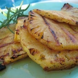 Grilled pineapple slices topped with fresh rosemary sprigs on a plate