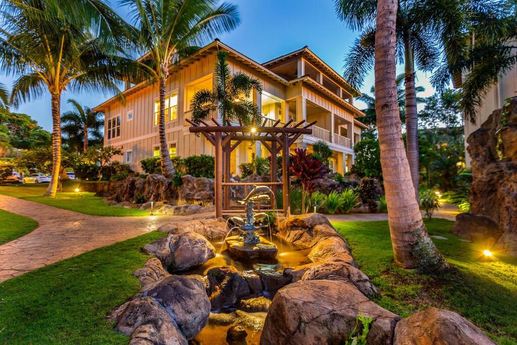 A stunning home in Kauai Villas, featuring a serene waterfall and lush palm trees.